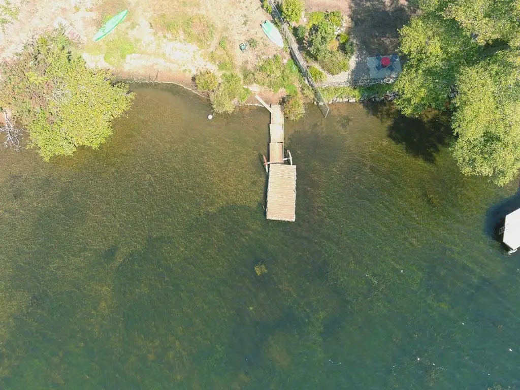 Aerial view of a dock extending into a lake, with a kayak onshore, surrounded by trees and greenery.