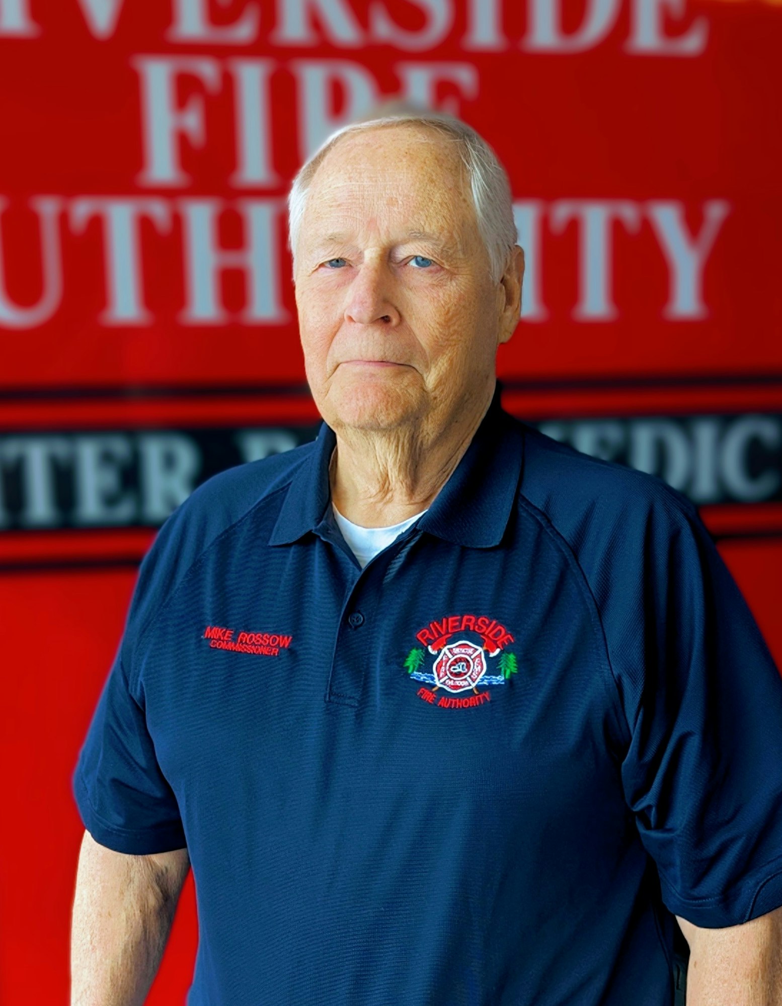 An older man in a uniform with a fire authority logo in front of a red background.