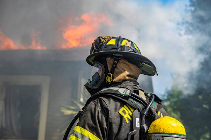 Firefighter in gear observing a blaze at a building.
