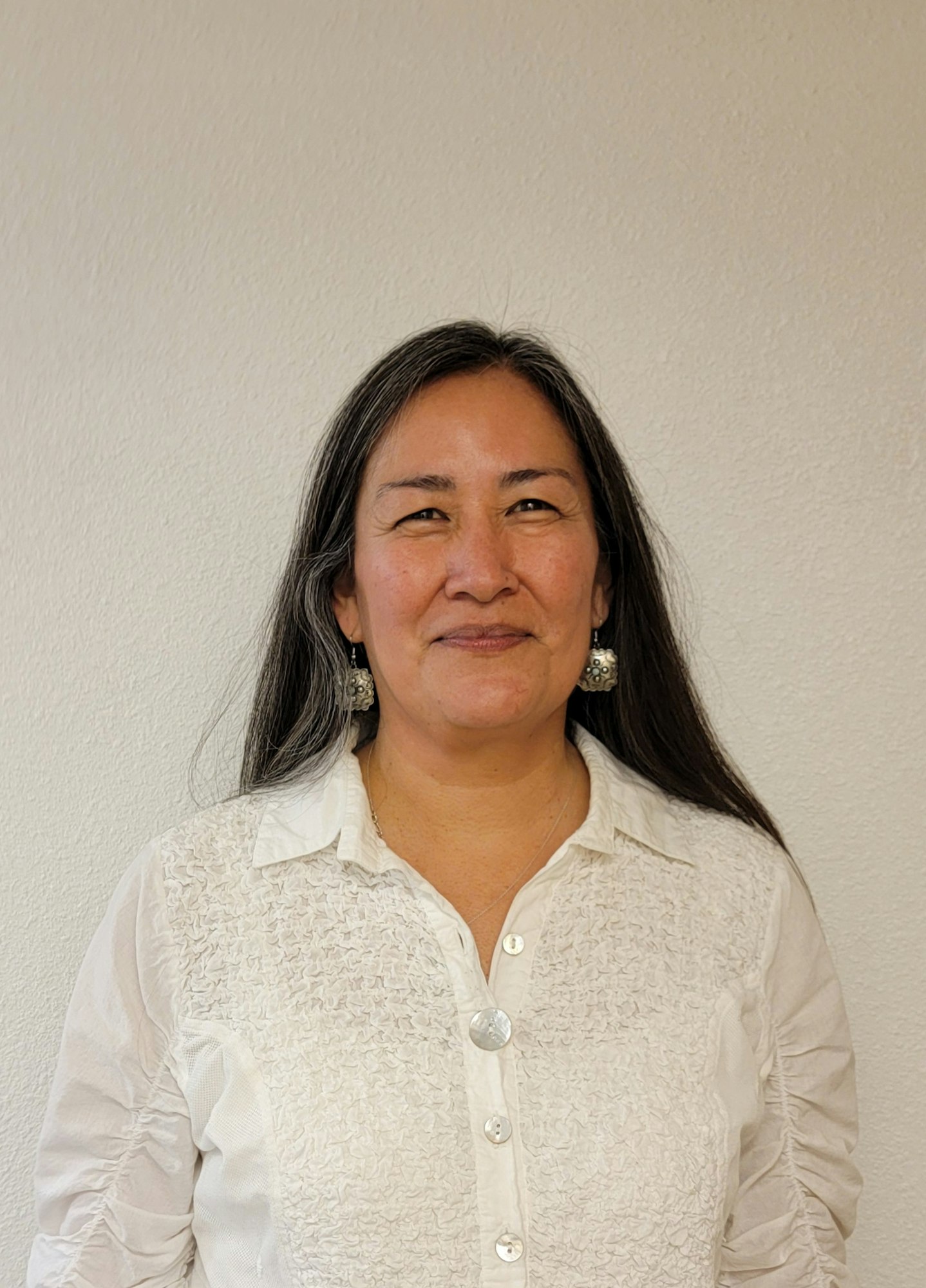 A person with long, dark hair is smiling and wearing a white shirt.