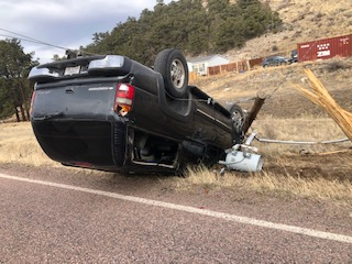 An overturned black vehicle beside a broken utility pole, suggesting a road accident.