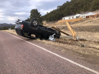 Overturned car beside road with broken utility pole.
