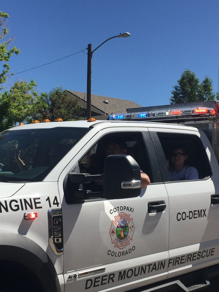 A fire rescue vehicle with flashing lights and "ENGINE 14" written on it. There are people inside, and it's a sunny day.