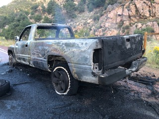 A burned-out truck by the roadside, missing tires and heavily damaged.