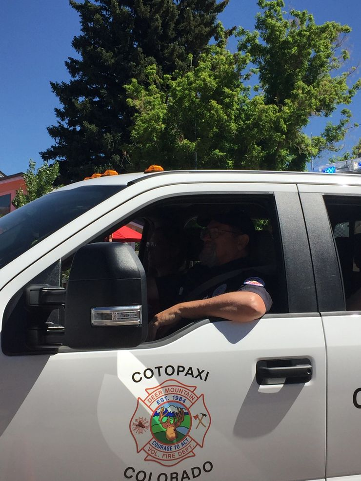 A person in a Cotopaxi Volunteer Fire Department vehicle with trees in the background.