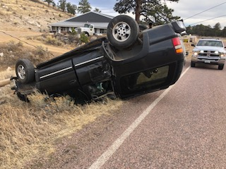 An overturned car by the side of a road with another vehicle in the background.