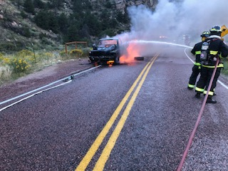 Firefighters are extinguishing a burning vehicle on a road.