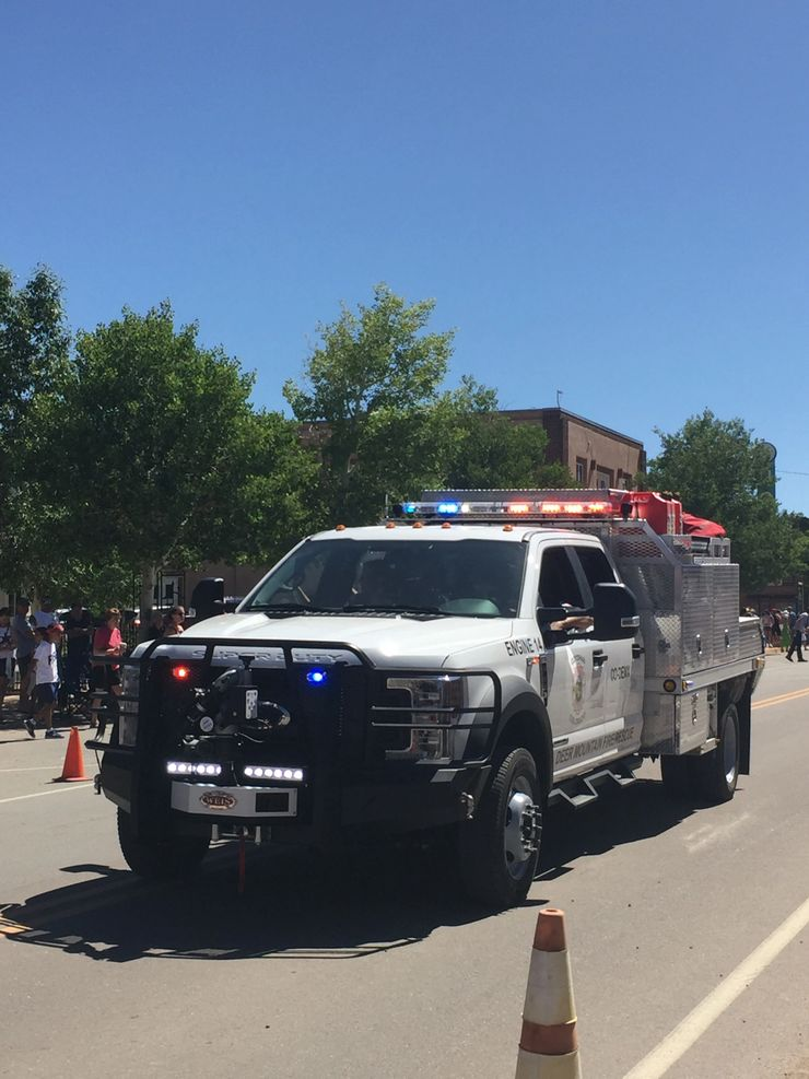 A fire department vehicle with flashing lights in a parade, with spectators on the roadside.