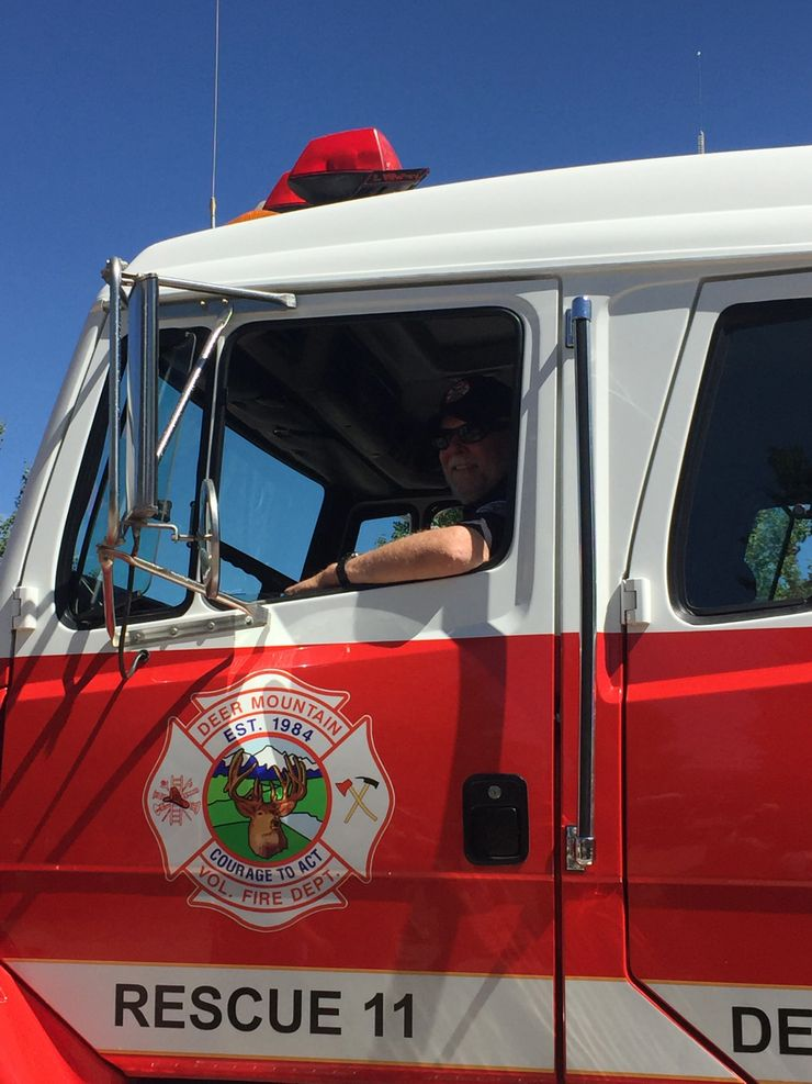 A firefighter inside a red rescue firetruck labeled "RESCUE 11" from the Deer Mountain Volunteer Fire Department.