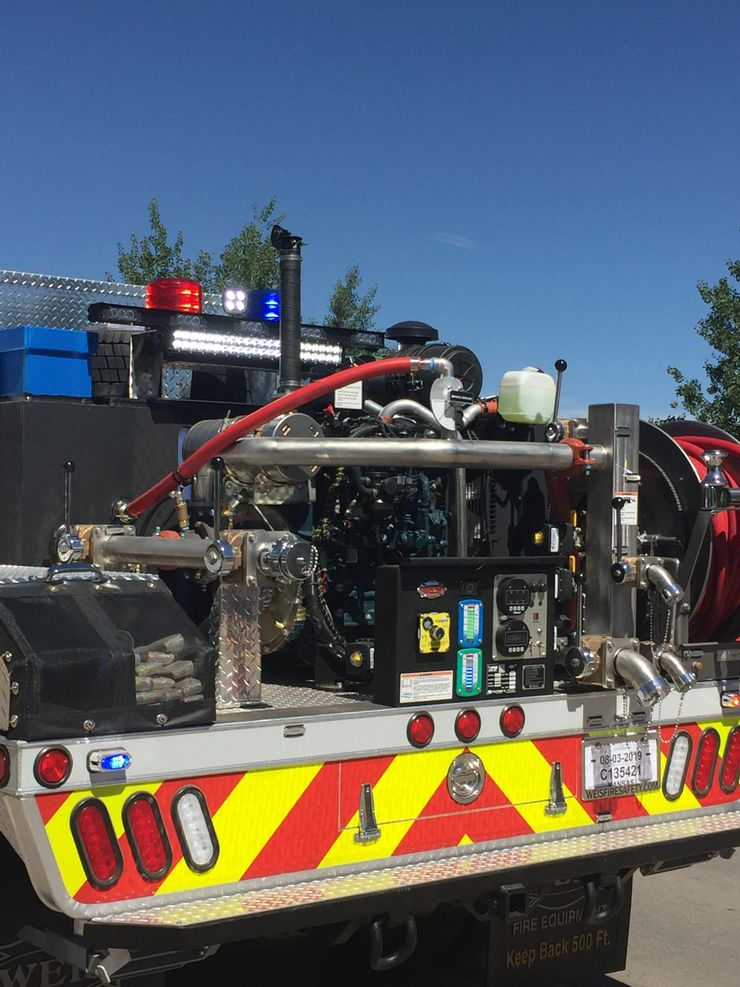 A fire truck's detailed rear view with hoses, pumps, controls, and emergency lights.