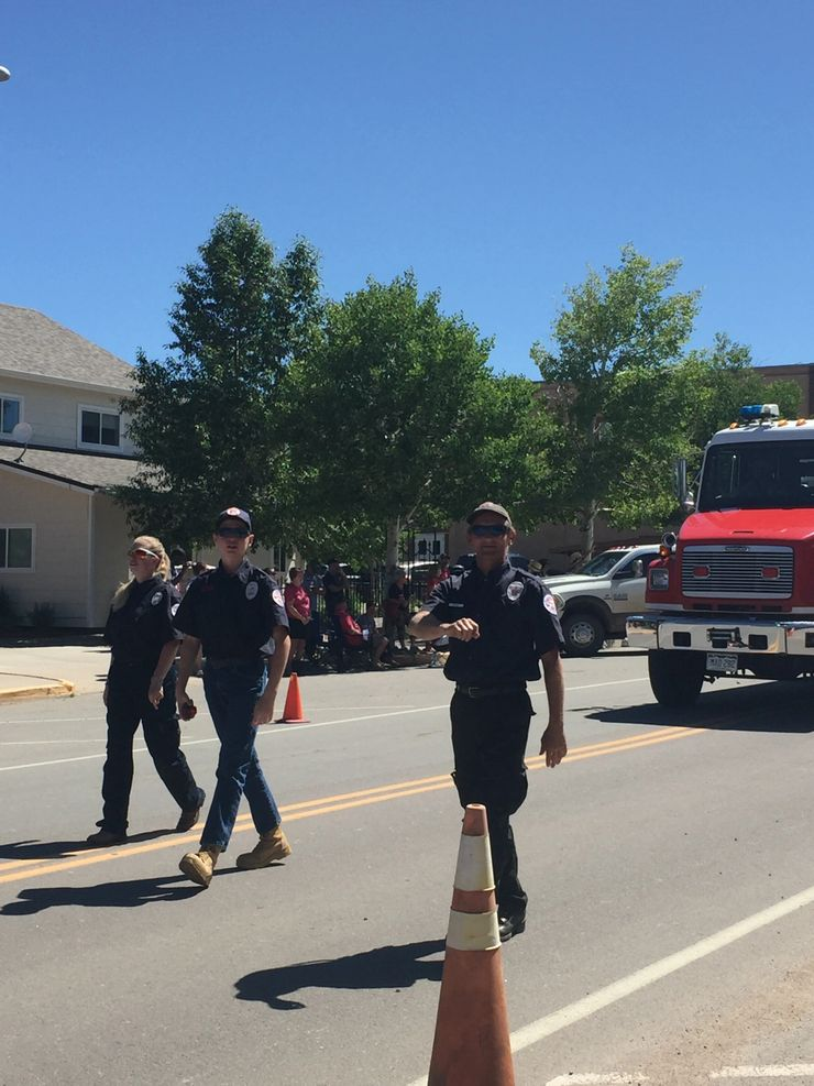 Three firefighters walking, a fire truck in the background, people watching, clear day.