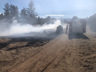 A vehicle emitting smoke on a dirt road with trees in the background.