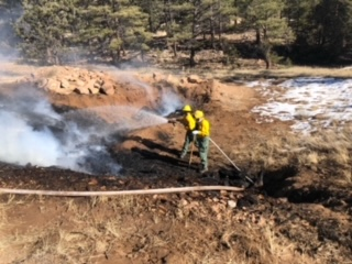 A firefighter is hosing down a smoky area with snow on the ground.