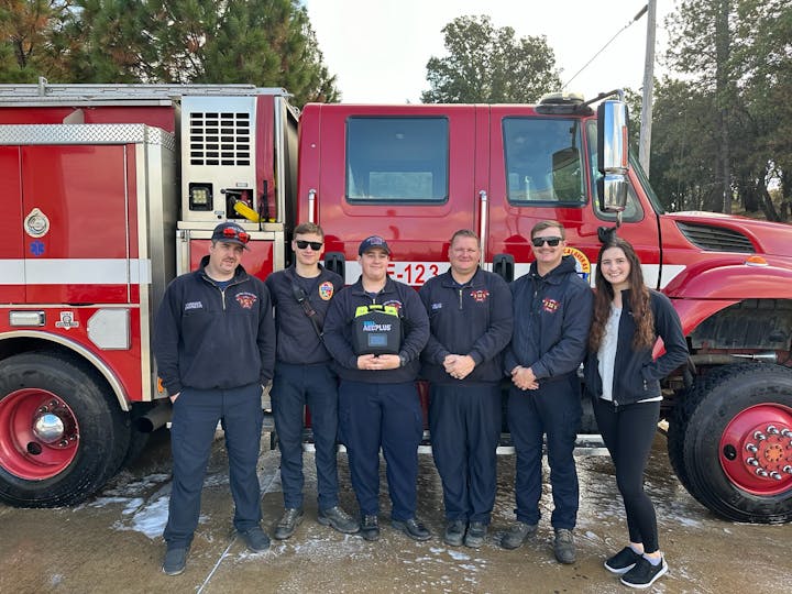 Group of firefighters posing in front of a red fire truck.