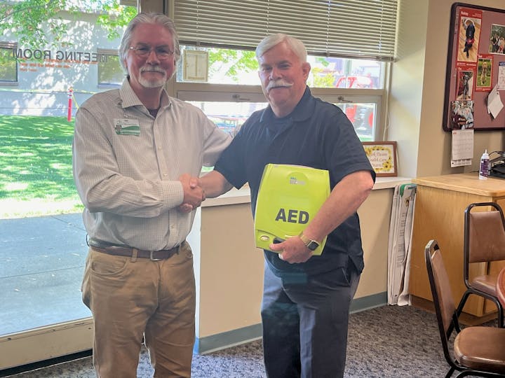 Two men shaking hands; the one on the right holds an AED device.