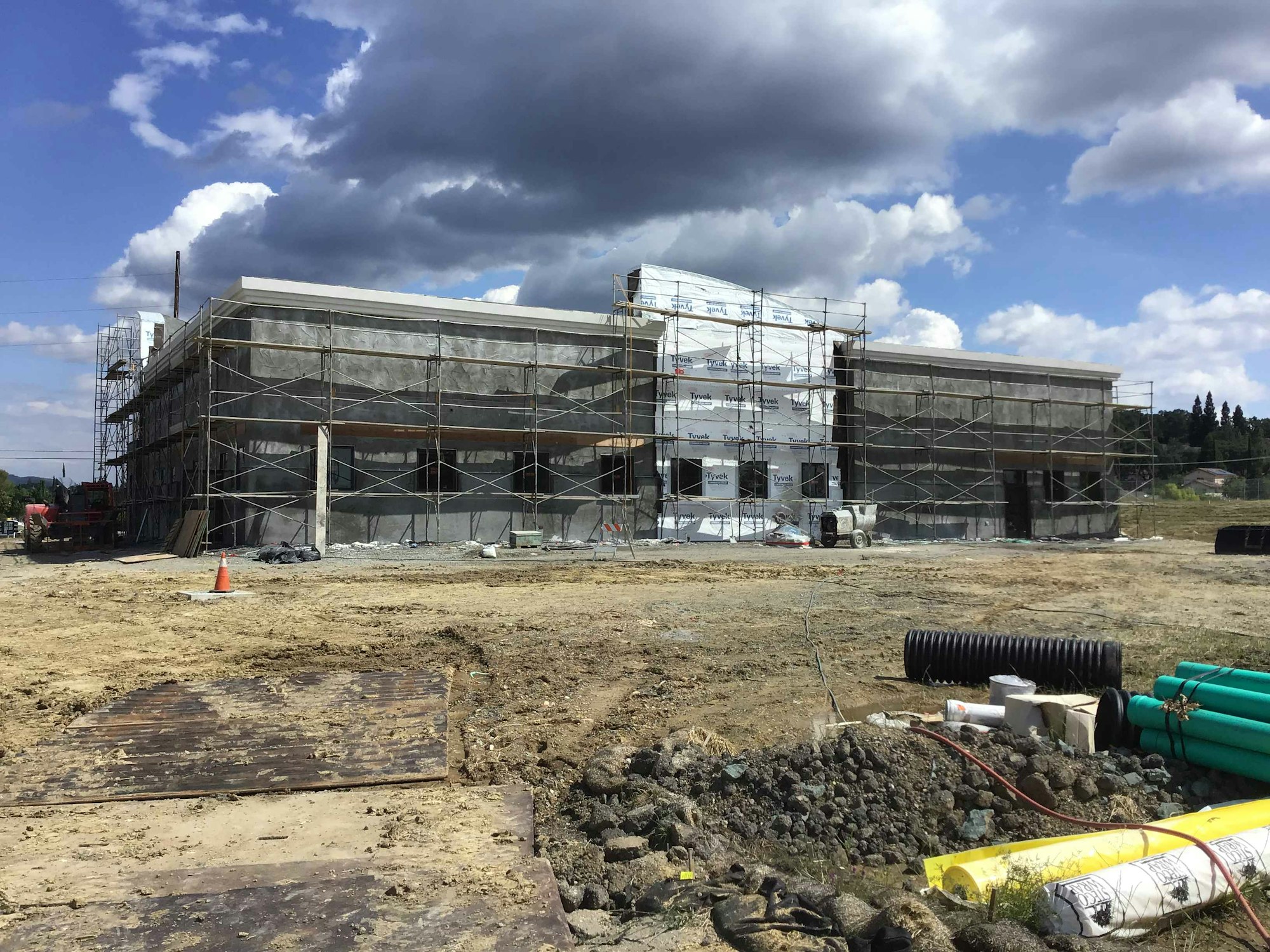 A partially constructed building surrounded by scaffolding, with construction materials and equipment nearby.
