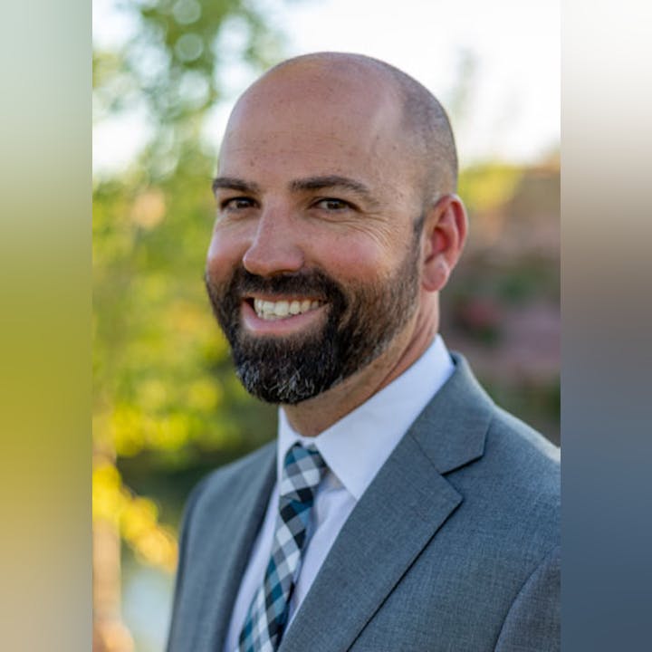 A smiling man with a beard, wearing a gray suit and a striped tie.
