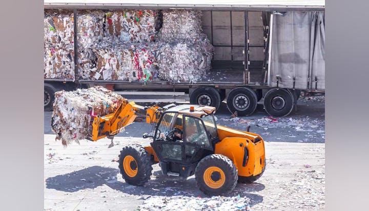 A forklift carrying a bale of recycled materials near a truck.