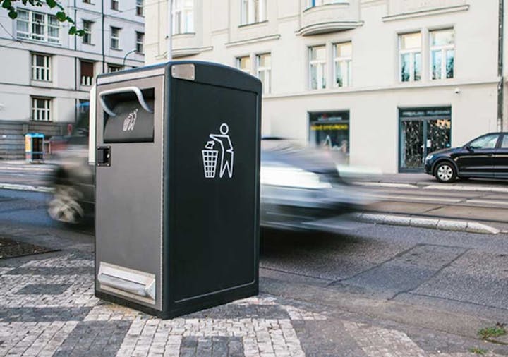 A modern, large trash bin on a city sidewalk with a blurred car passing by in the background.