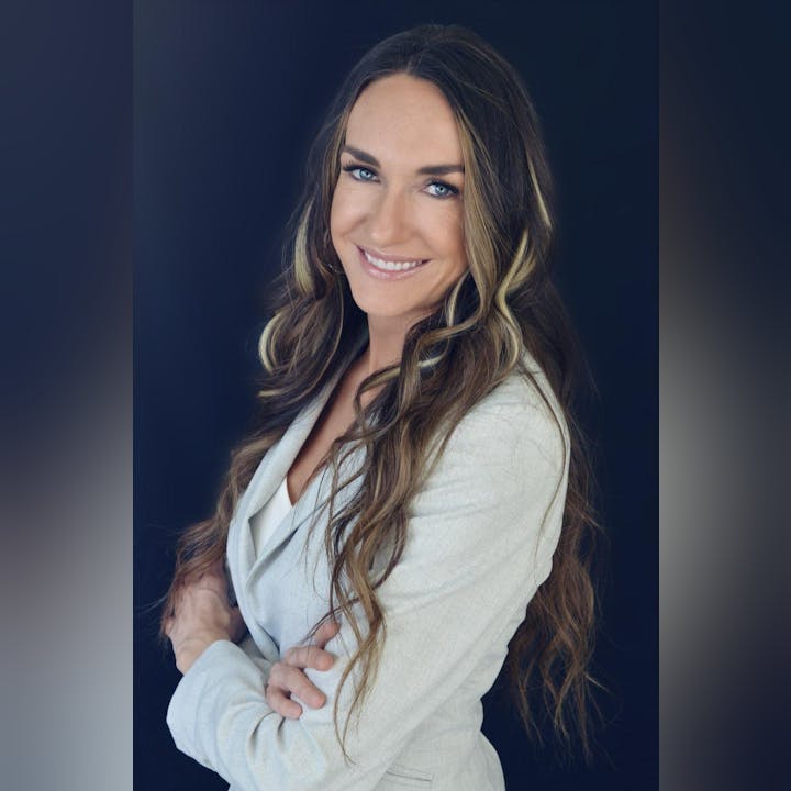 A smiling woman with long hair, wearing a white blazer, against a black background.