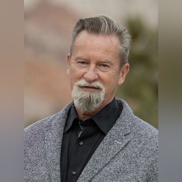 A man with a beard, wearing a grey coat and black shirt.