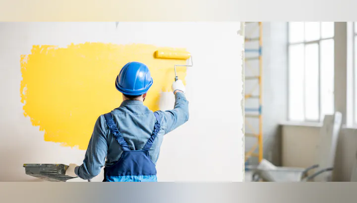 Person in a hard hat painting a wall yellow.