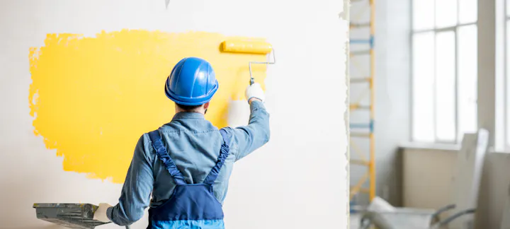 Person in a hard hat painting a wall yellow.