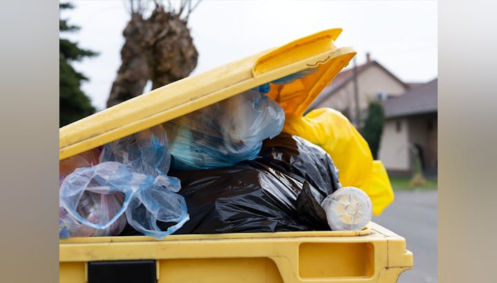 An overflowing yellow dumpster filled with bags of trash on a residential street.