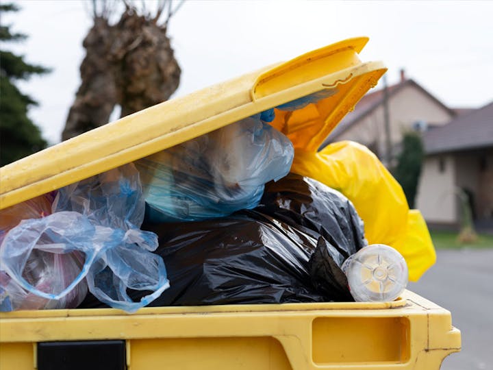 An overflowing yellow dumpster filled with bags of trash on a residential street.