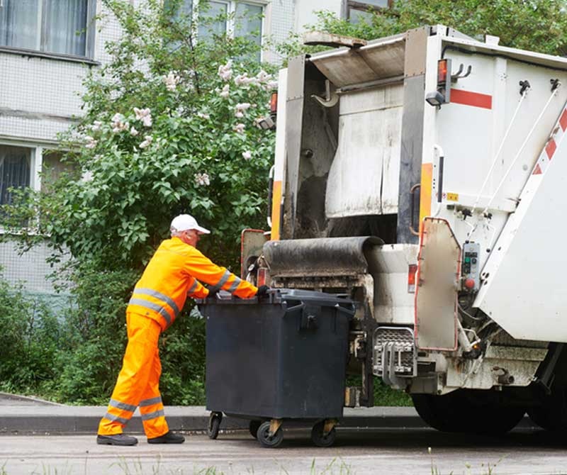 A person in a high-visibility outfit is emptying a trash bin into a garbage truck.