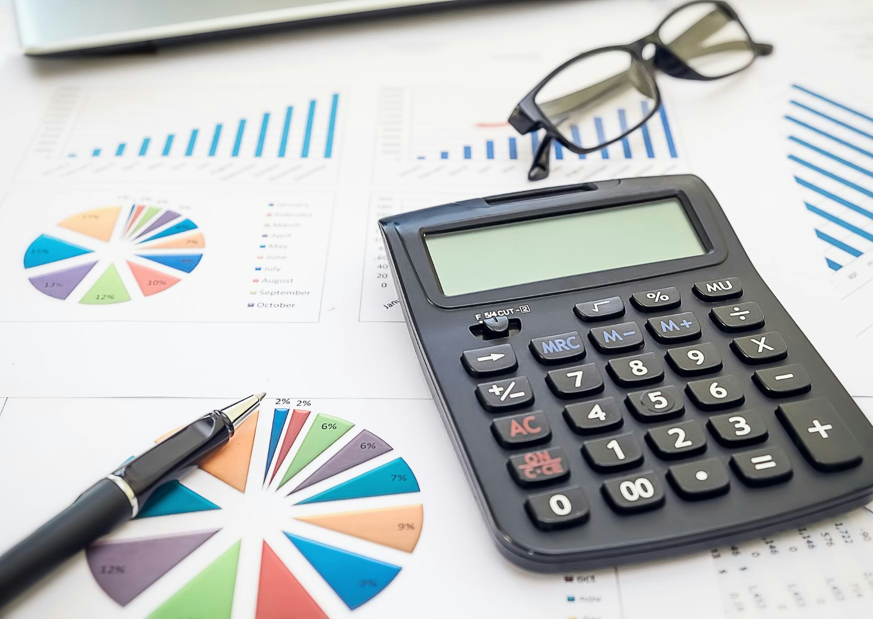 A calculator, pen, glasses, and printed charts on a table, signifying financial analysis or accounting.