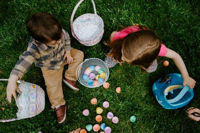 Two kids with Easter eggs and baskets on grass.