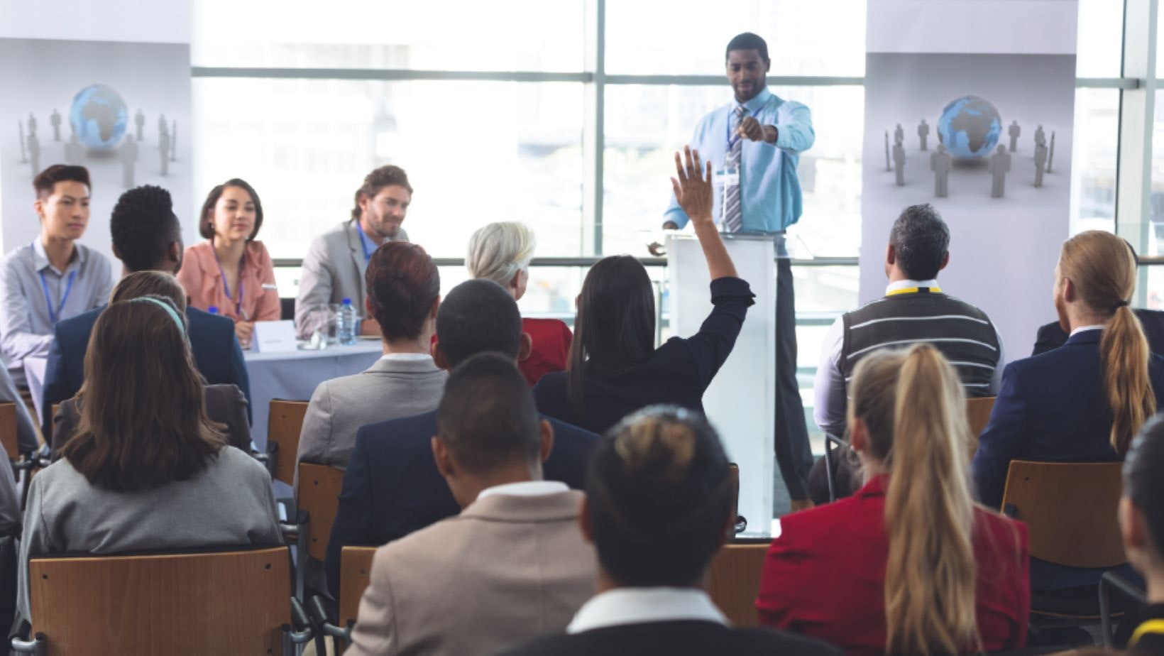 A presenter leading a meeting with a diverse group of attendees in a bright conference room.