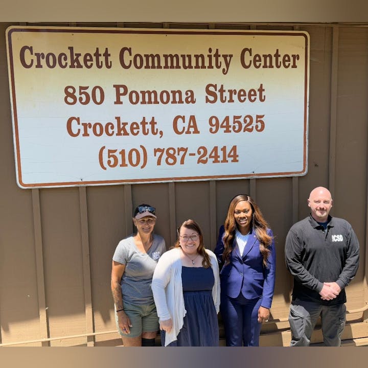 Four people standing under a sign for Crockett Community Center, 850 Pomona Street, Crockett, CA.