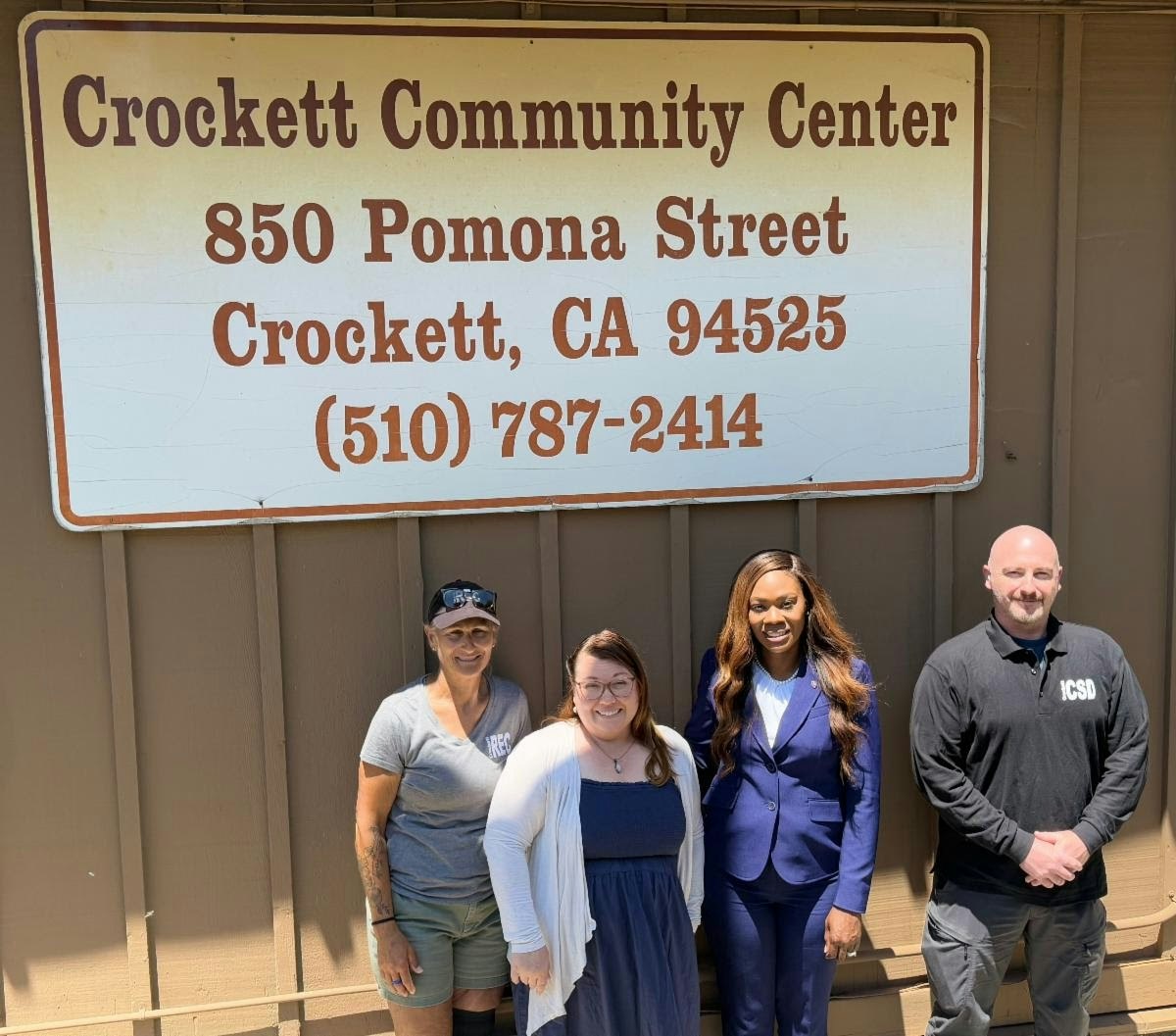 Four people standing under a sign for Crockett Community Center, 850 Pomona Street, Crockett, CA.