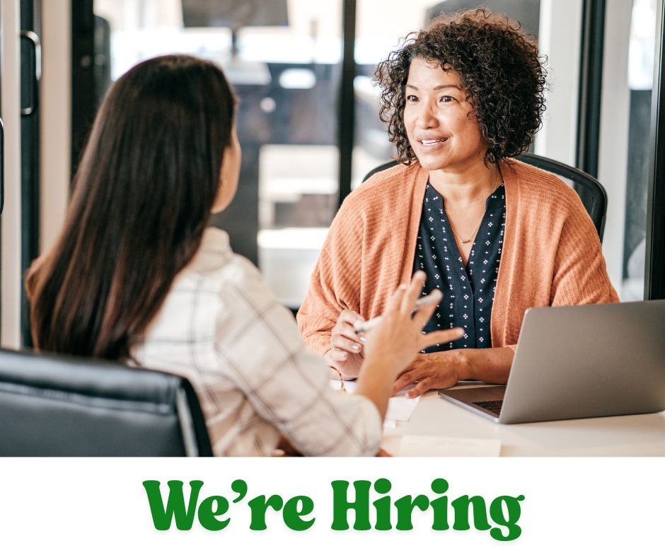 Two people engaged in a conversation at a desk with a laptop, with "We're Hiring" text below.