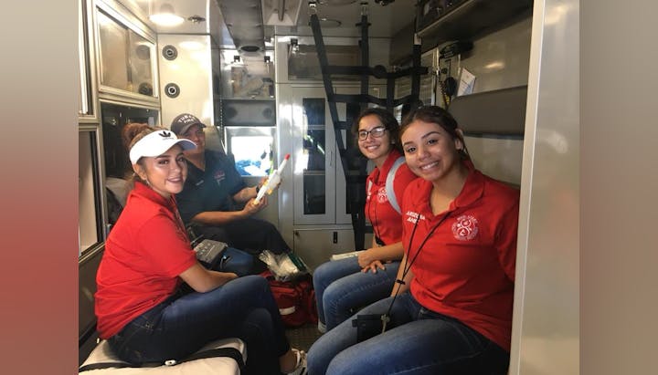 Four people in red shirts smiling inside a vehicle, possibly an ambulance or mobile clinic.