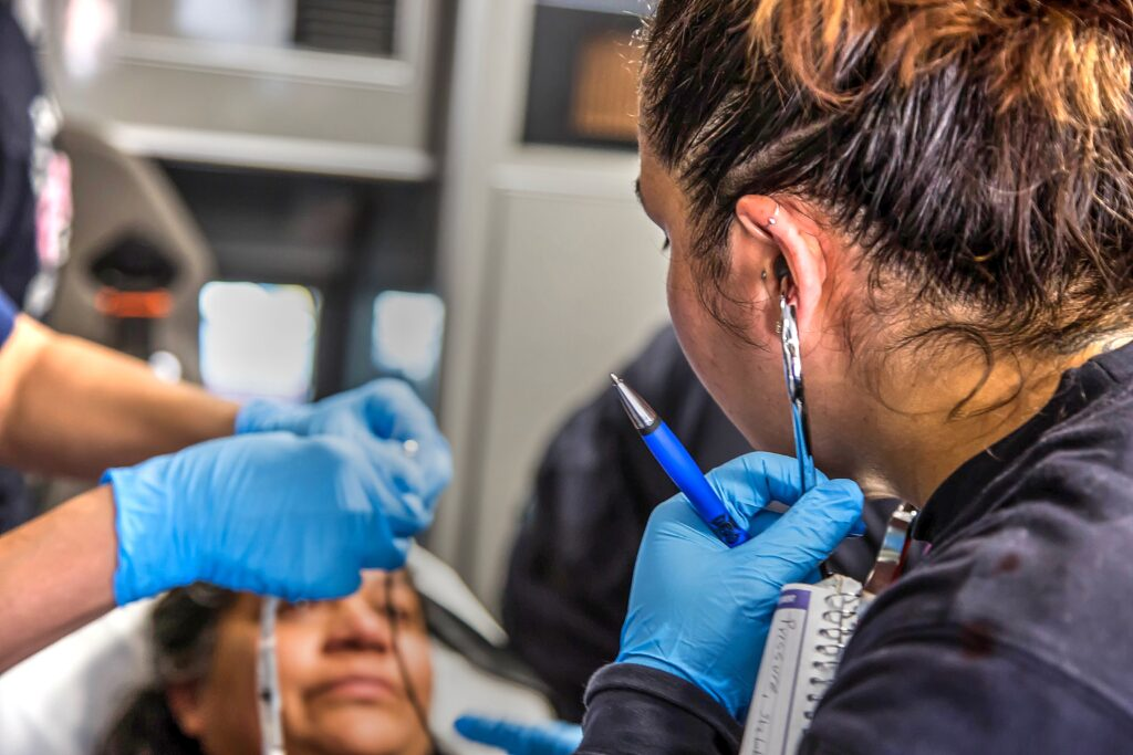Person in blue gloves using a tool near another person's ear, possibly a medical or piercing procedure.