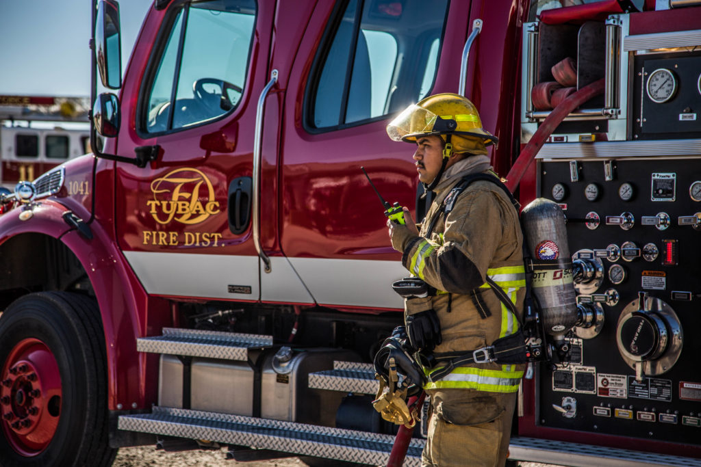 A firefighter beside a fire truck, holding a radio.