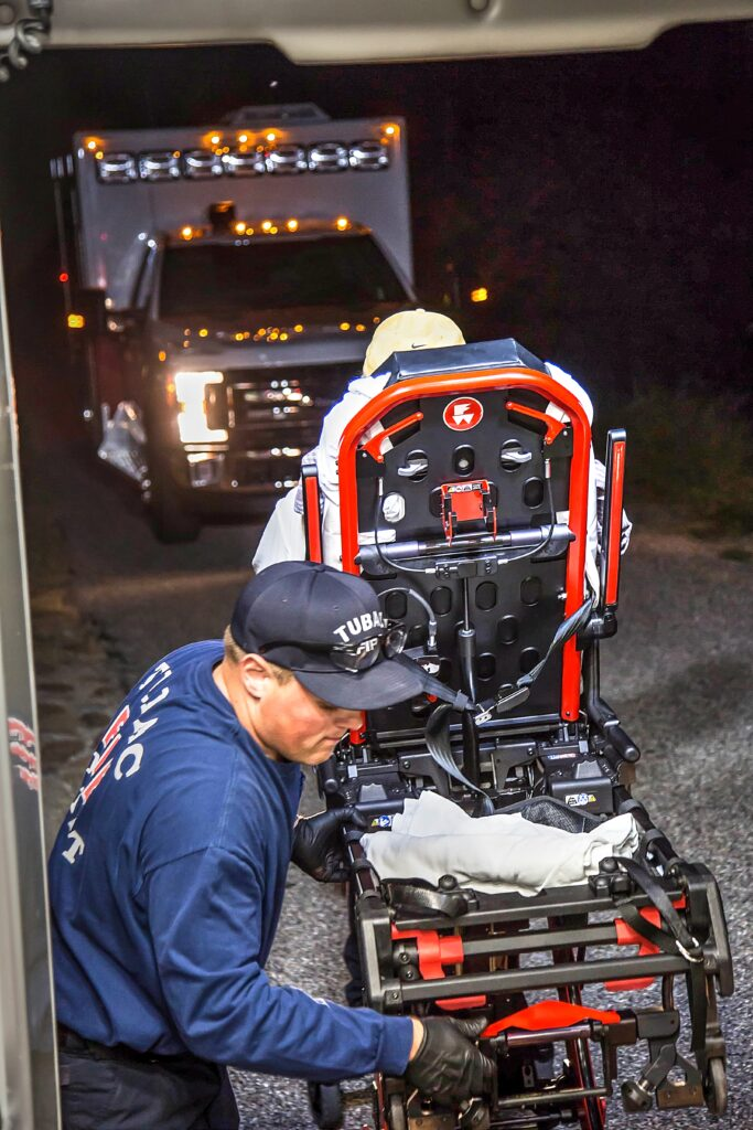 A paramedic is loading an empty stretcher into an ambulance at night.