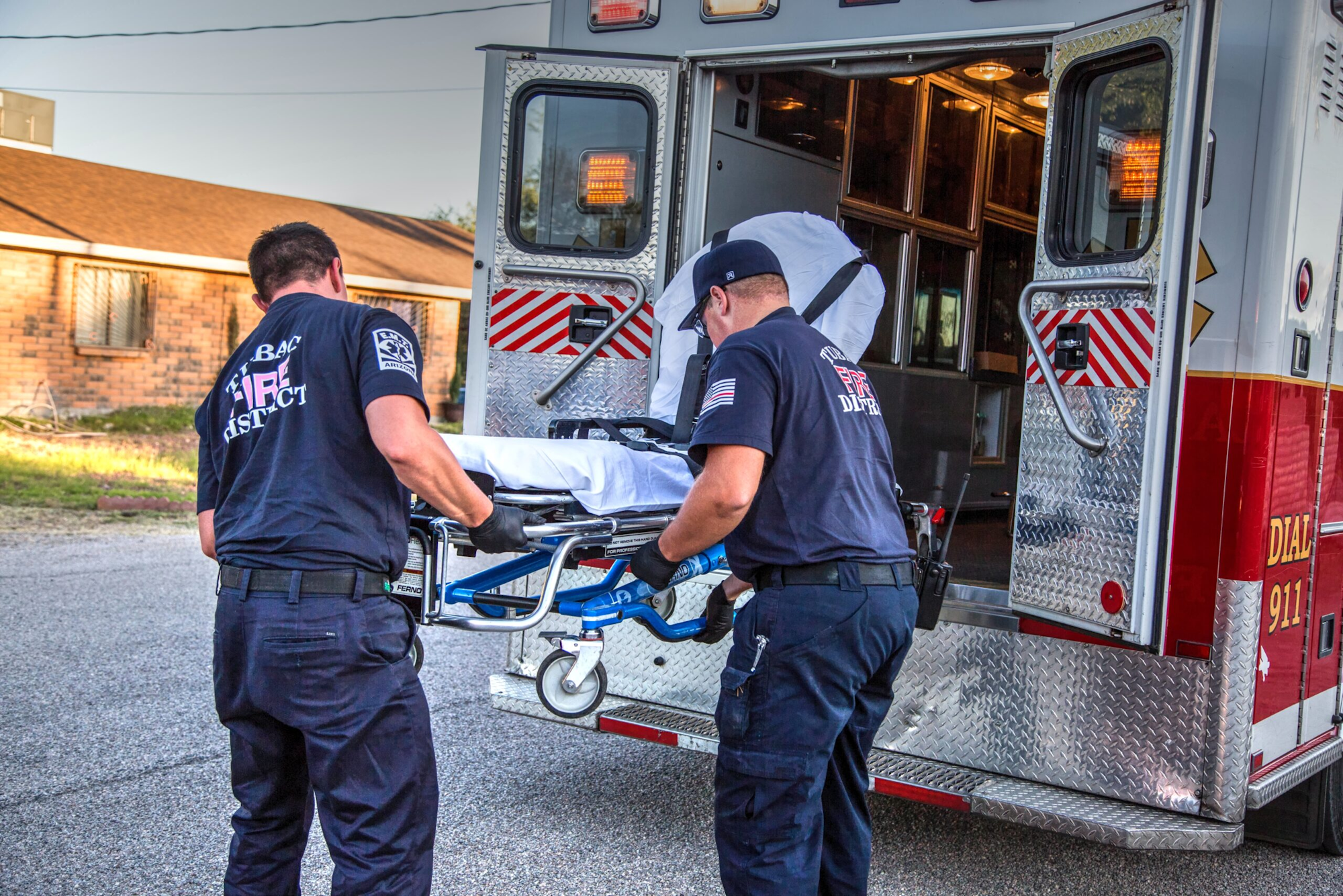 Paramedics loading a stretcher into an ambulance.