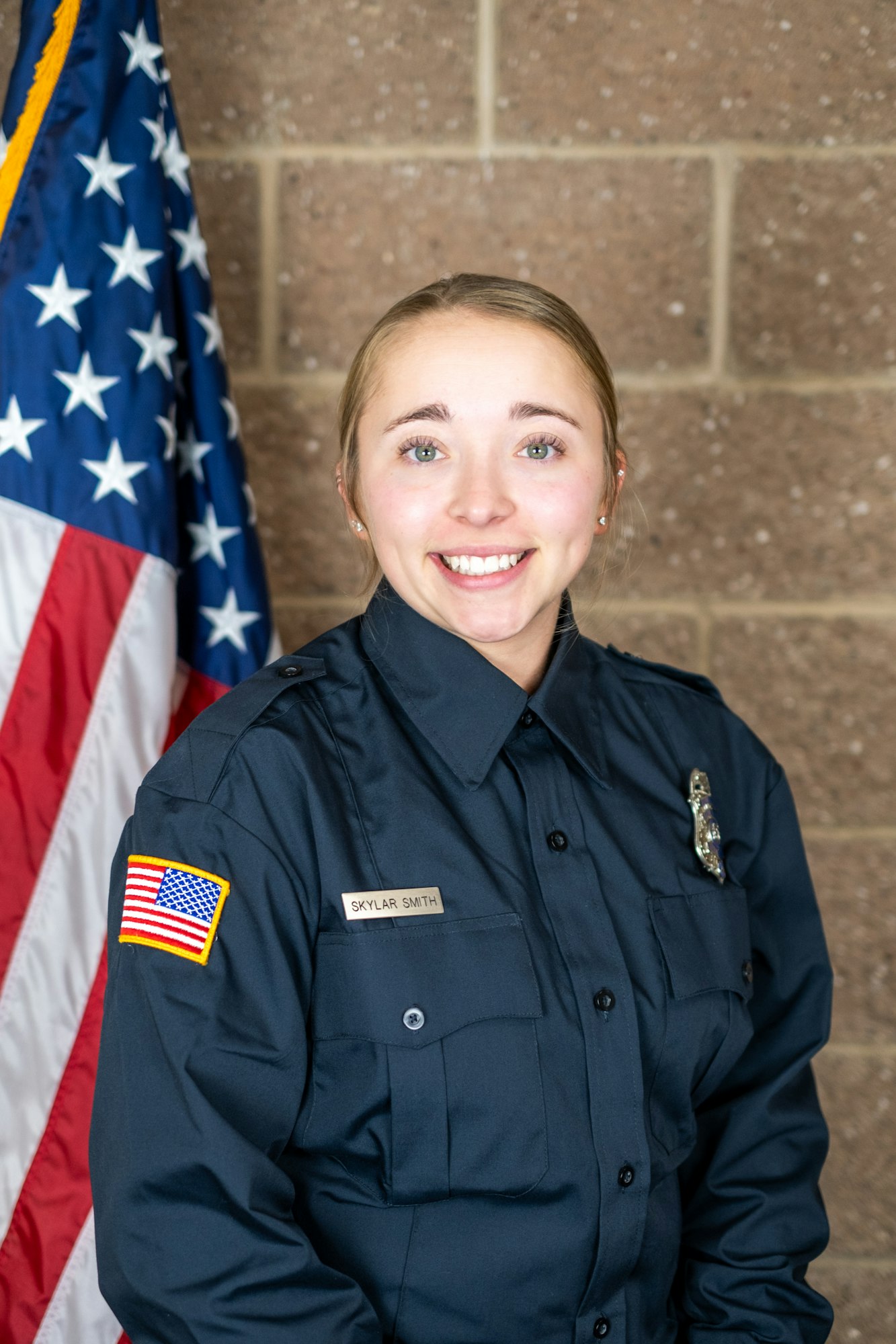 Person in uniform with name tag "SKYLAR SMITH" and a U.S. flag patch, standing beside an American flag.
