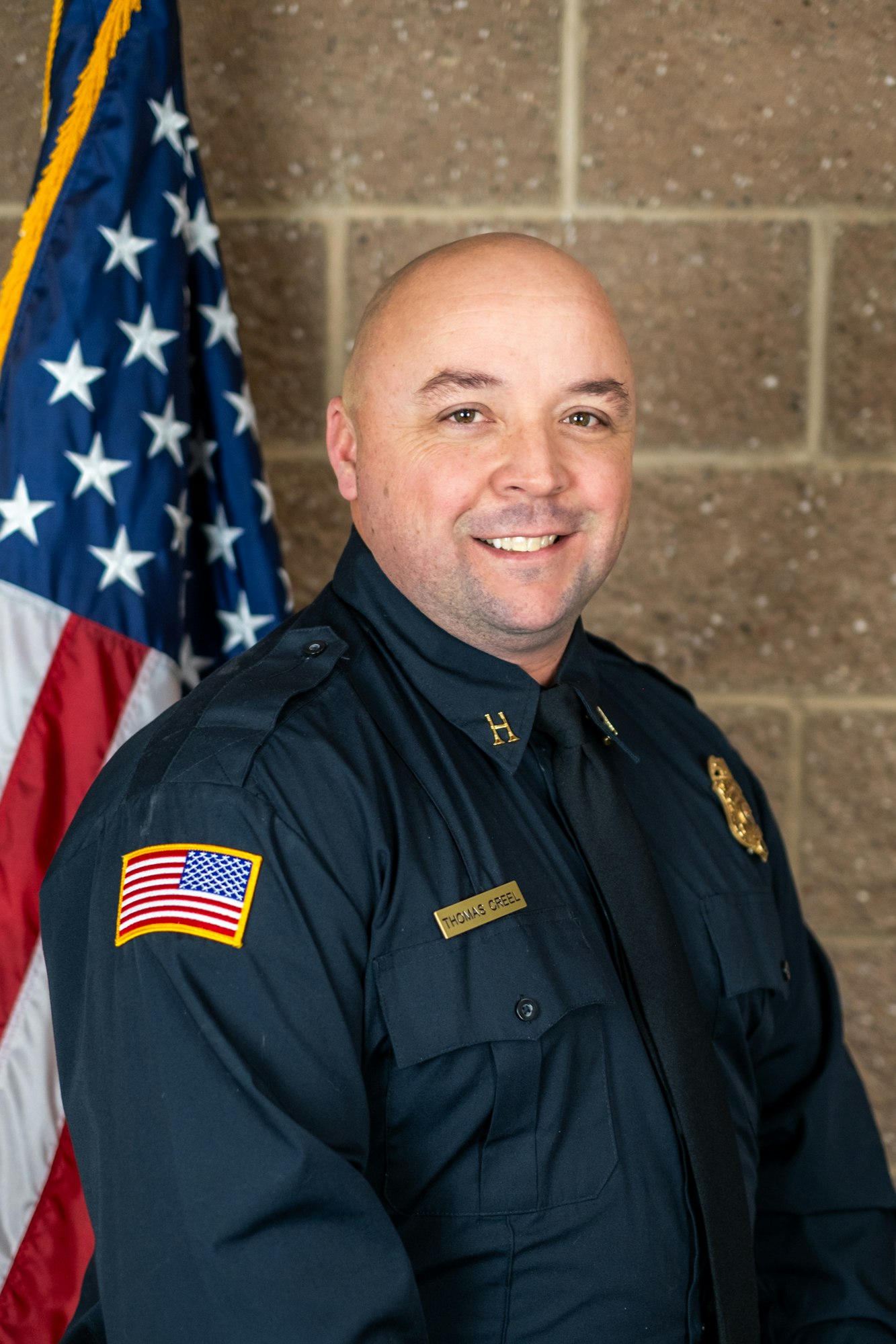 A uniformed officer smiling in front of a U.S. flag.