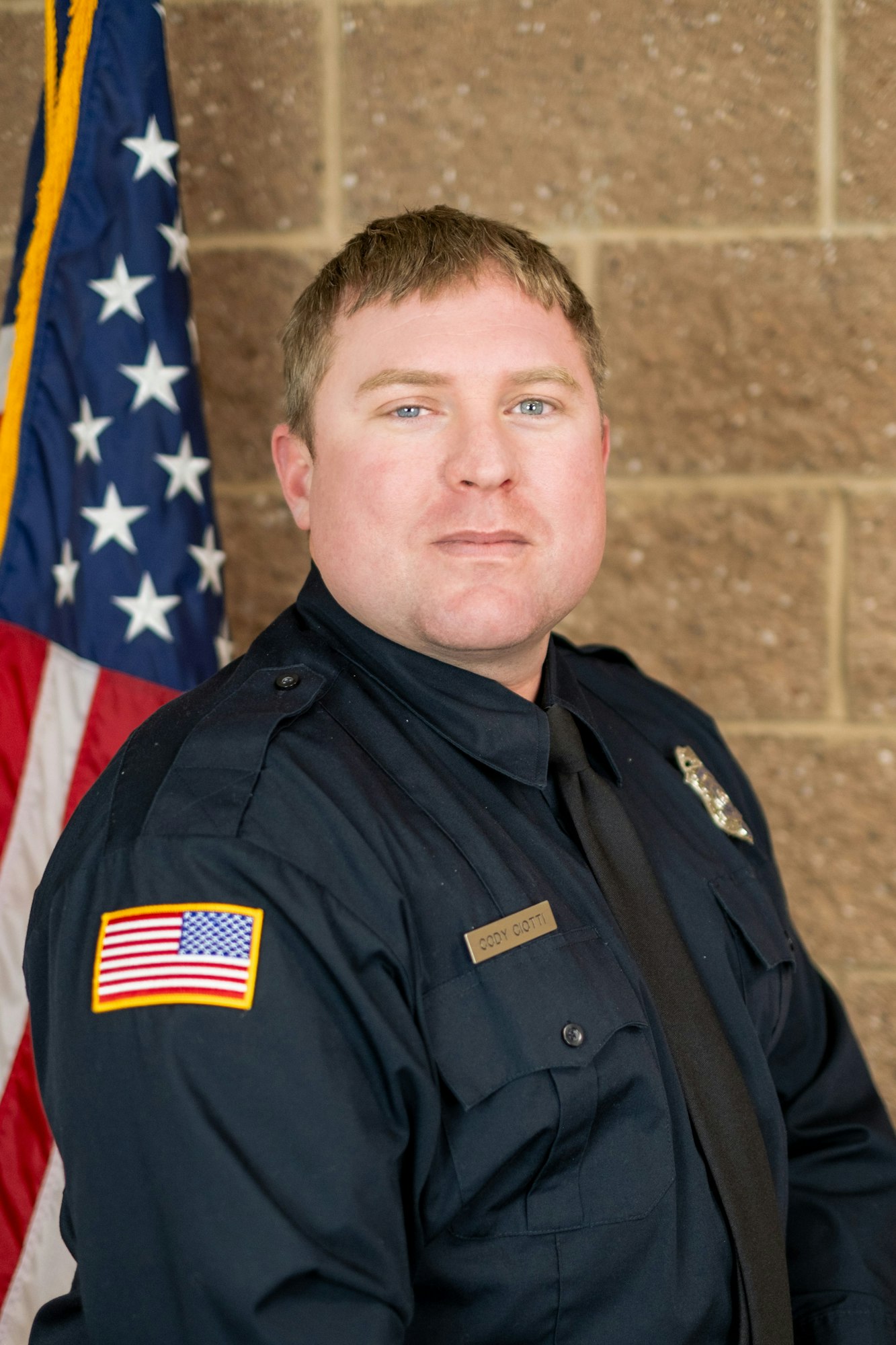 A person in a police uniform with an American flag in the background.