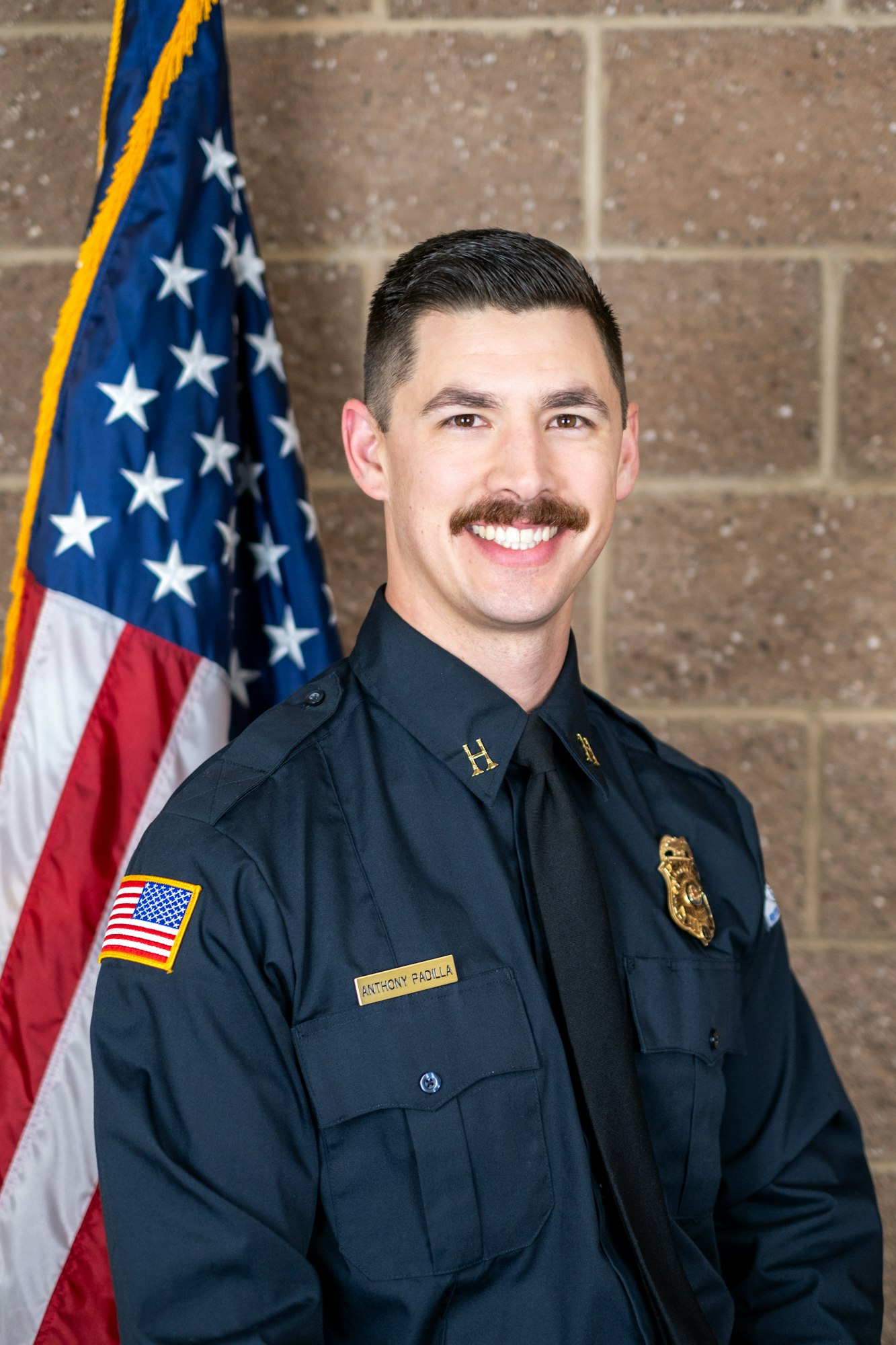 A man in uniform stands smiling in front of an American flag.