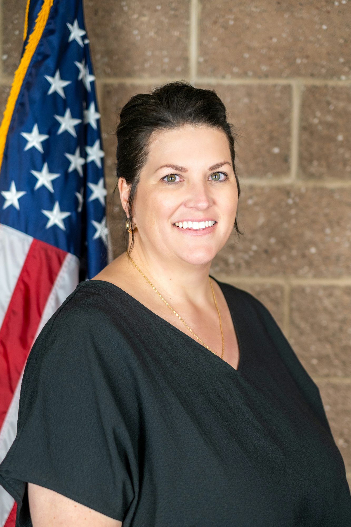 A person smiling in front of an American flag, wearing a black top.