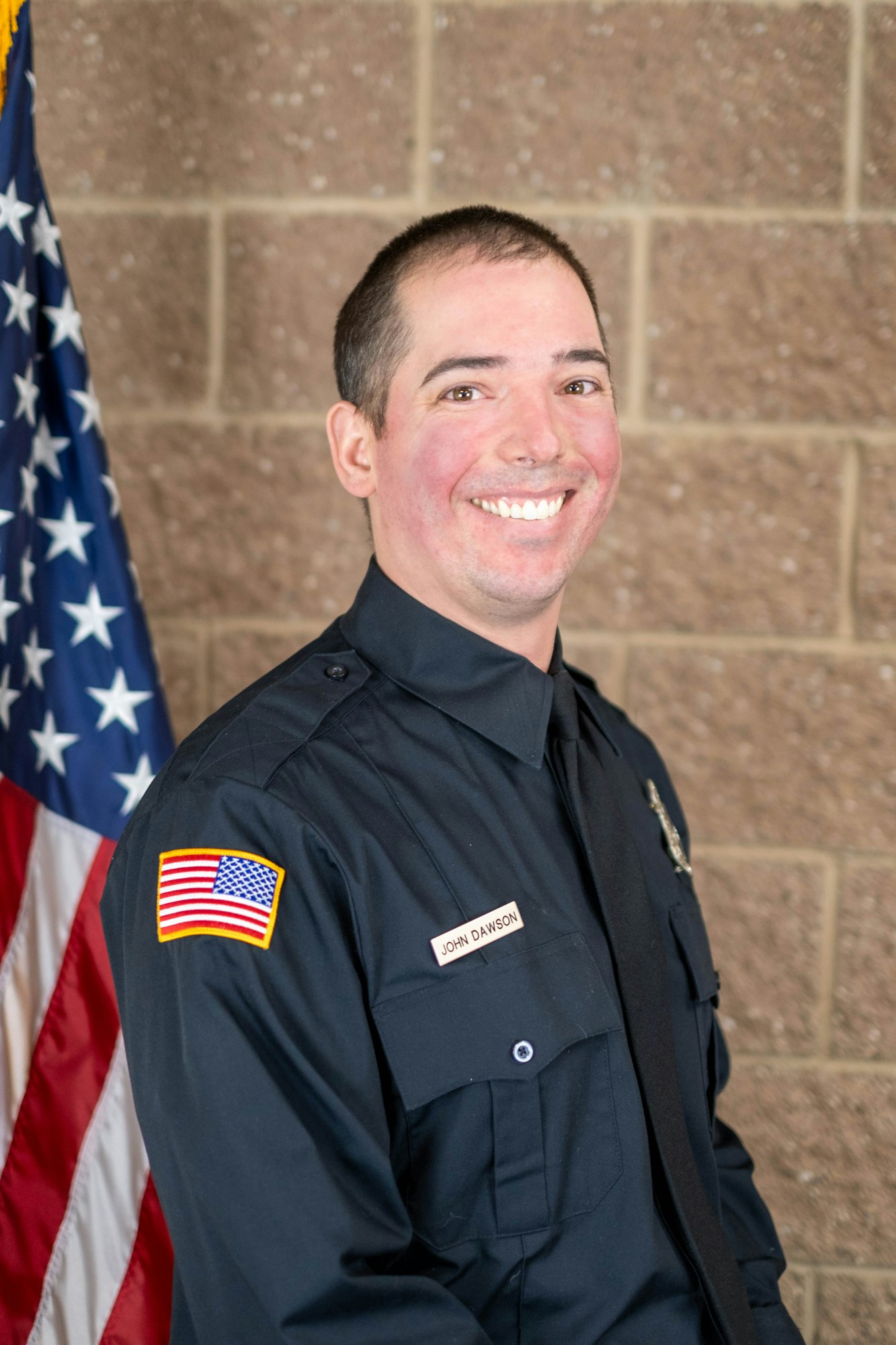 A smiling person in a uniform with an American flag in the background.