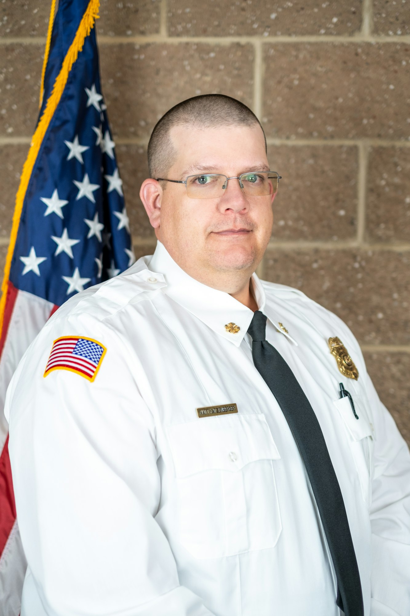 A person in a white uniform with an American flag patch, standing in front of a flag.