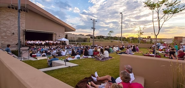 Outdoor concert with an audience seated on grass, enjoying music at sunset.