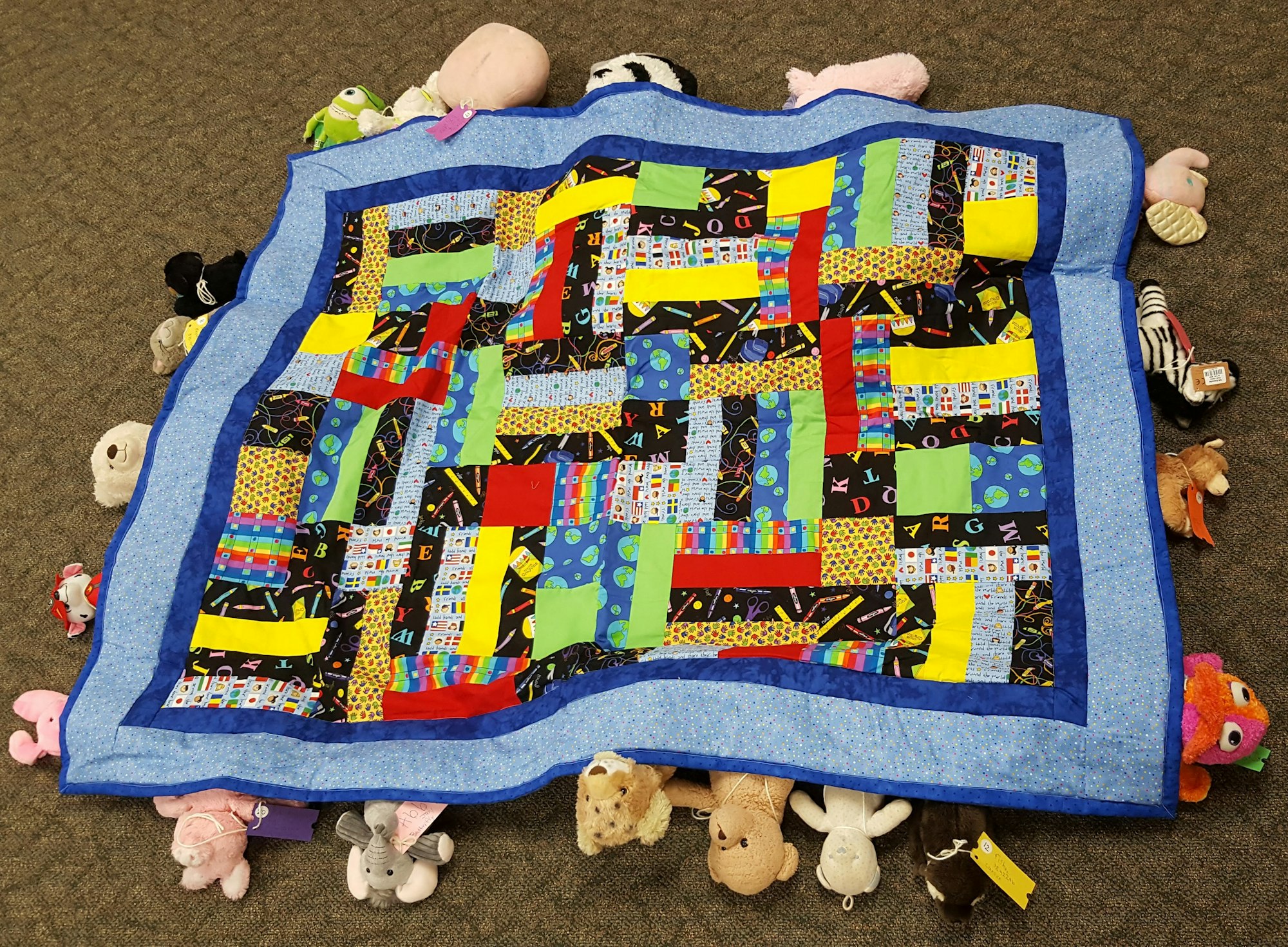 A colorful patchwork quilt surrounded by various stuffed animals.